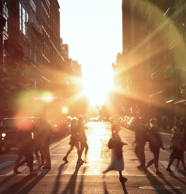 The sun at golden hour in midtown Manhattan, perfectly aligned between the buildings, as pedestrians cross the intersection.