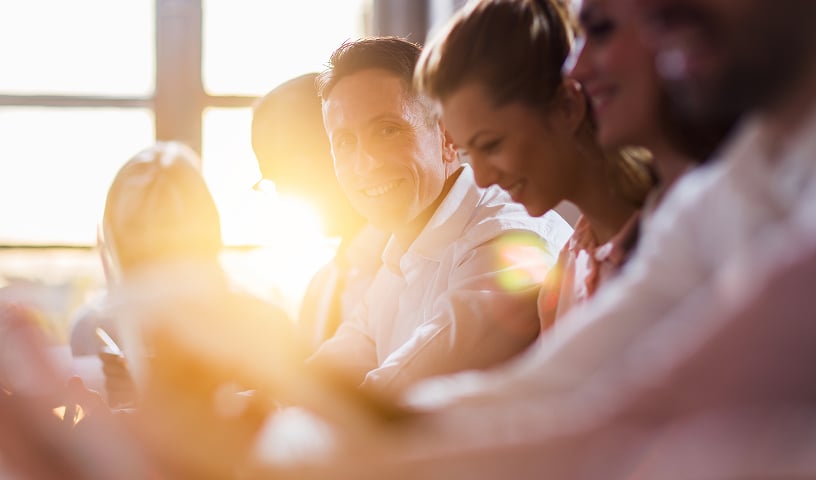 Closeup of six young professionals at a table, with the sun shining through the office window behind them.